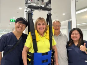 Patient Story Profile Picture - Dominique standing in harness with therapy team at Verita Neuro
